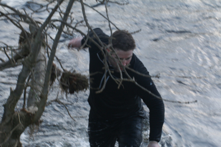 man wades through a river to fetch a cricket ball, the fast flowing water up to his waist