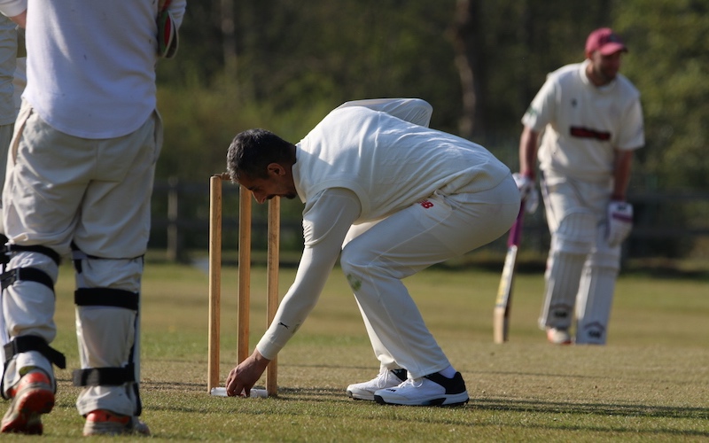 bowler picks up hand sanitiser behind the stumps in a game